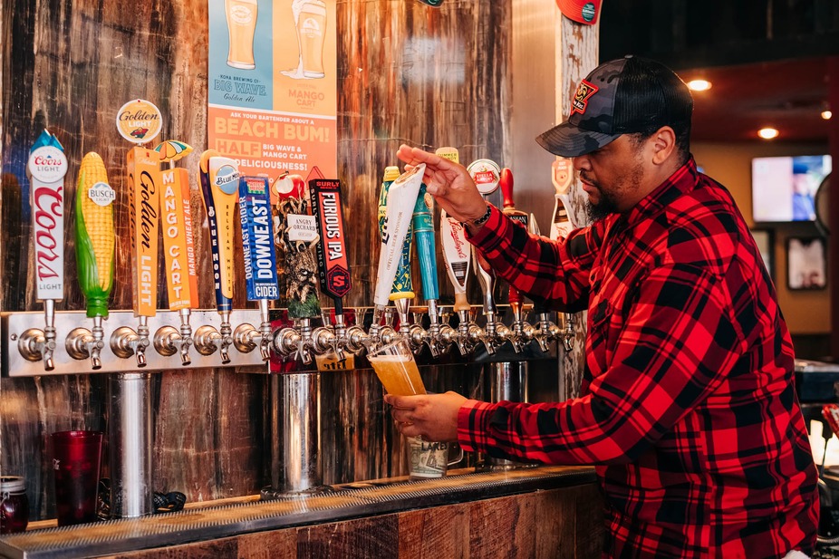 man in a red and black flannel shirt pouring beer from a tap on the wall.