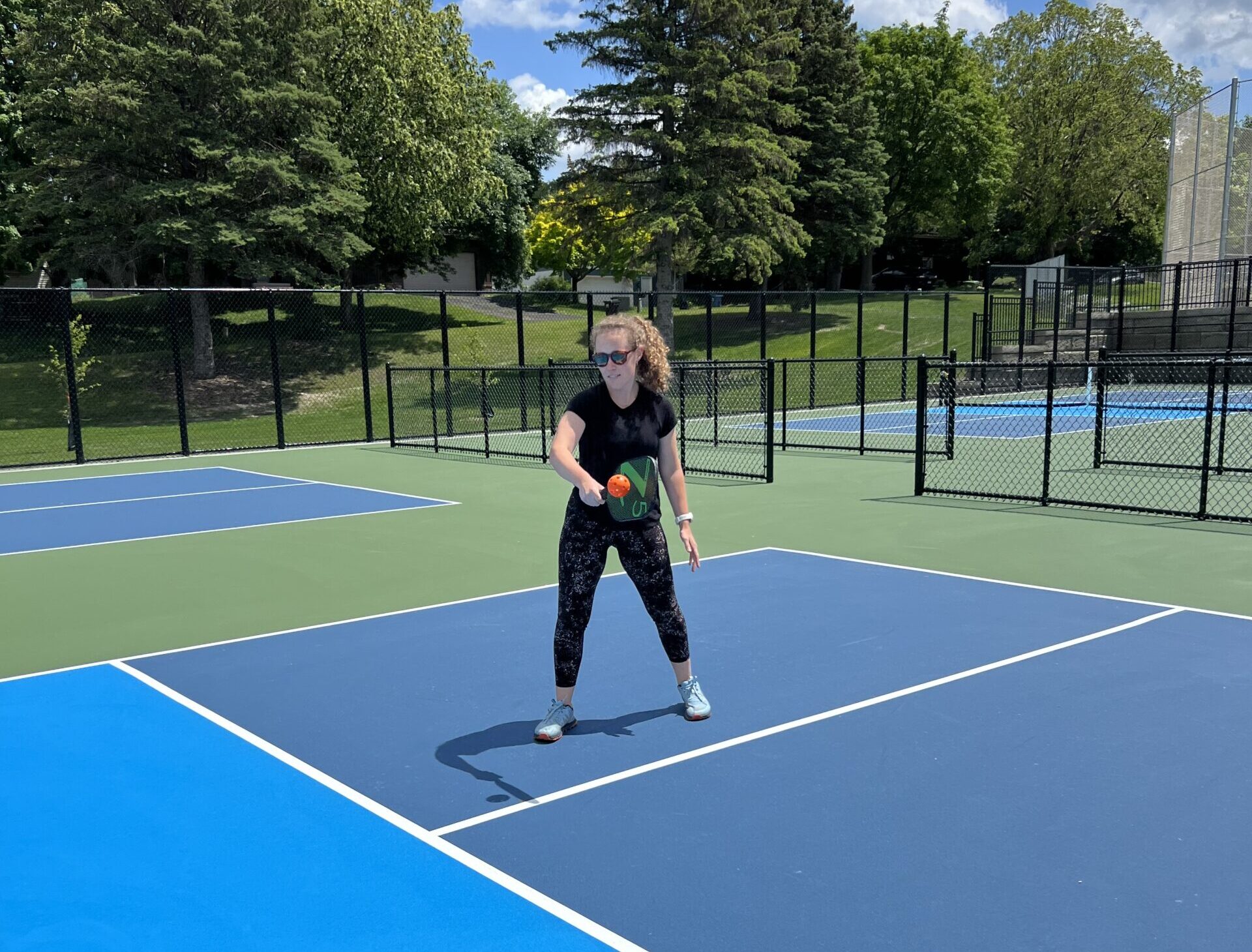 woman standing on a blue pickleball court ready to serve the ball.